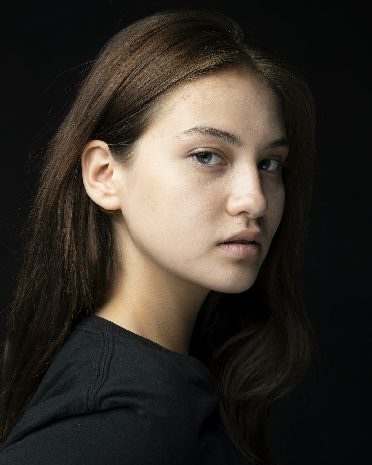 Portret mlade žene duge tamne kose na crnoj pozadini