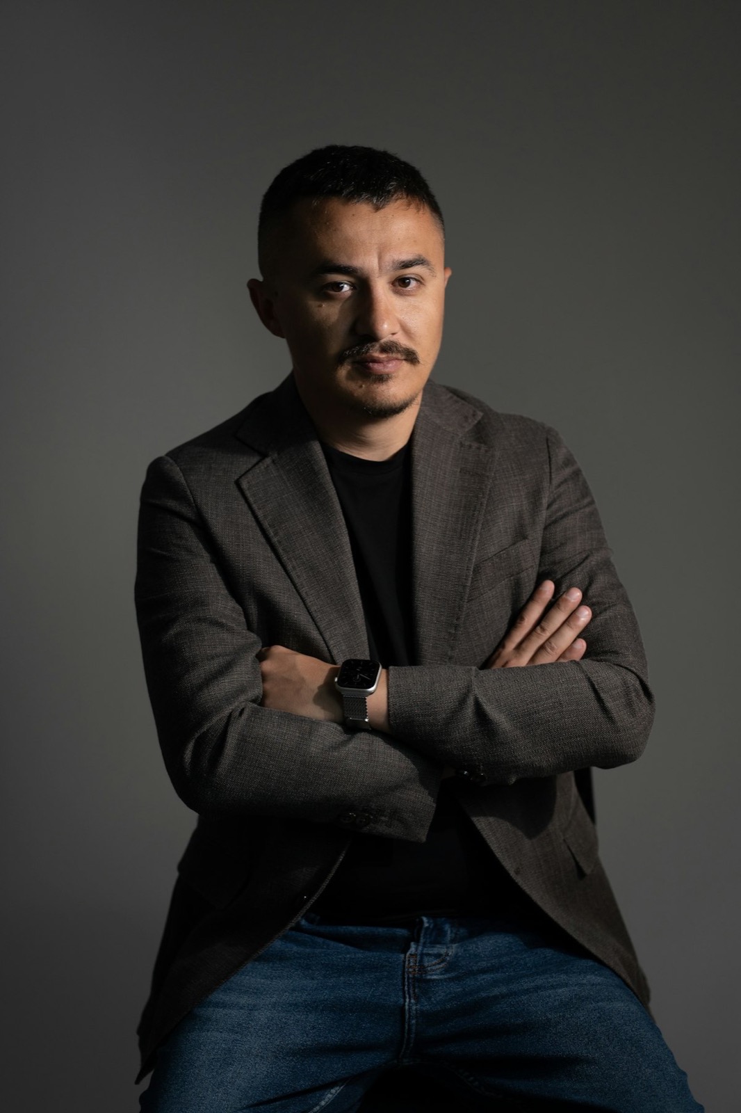 Muškarac u sakou prekrštenih ruku, poslovni portret na sivoj pozadini