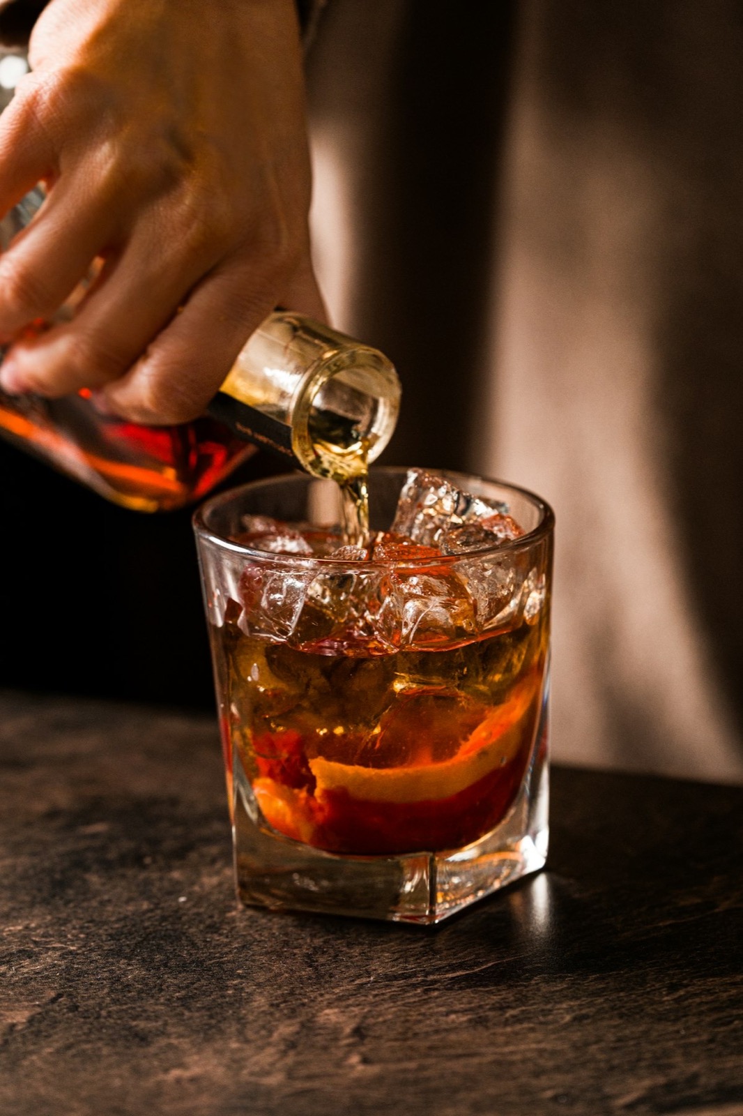 Barmen sipa ćilibarno piće u čašu sa ledom i korom pomorandže
